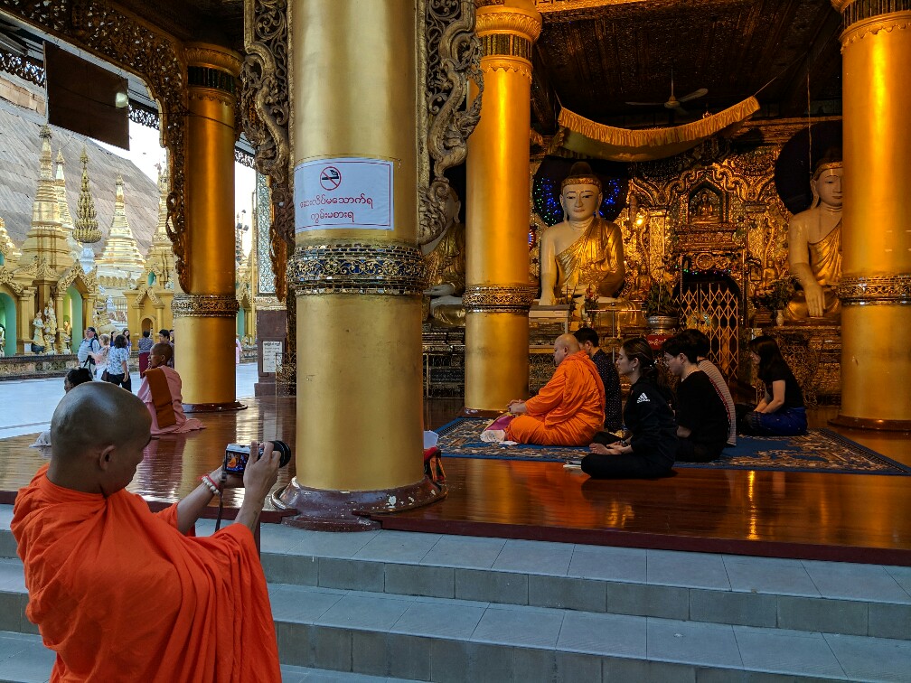 Moine prenant une photo d'un autre moine accroupi en train de prier