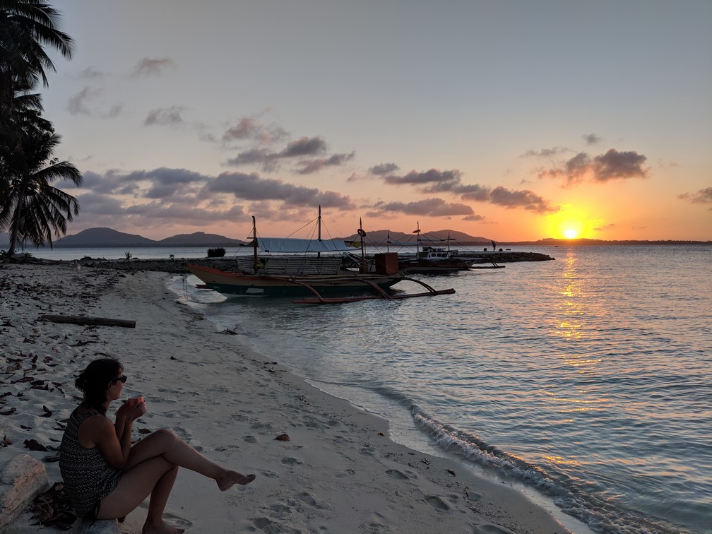 Salomé regarde le coucher de soleil assise sur la plage de l'île de Candaraman