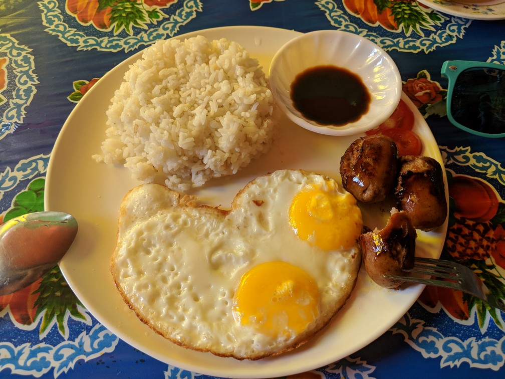 Une assiette avec des morceaux de saucisse, deux oeufs au plat en forme de coeur et du riz