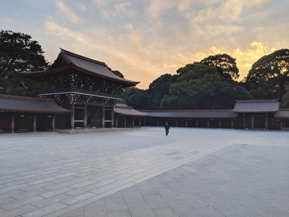 Gardien marchant seul dans la cour du Sanctuaire Meiji-Jingu, coucher de soleil derrière