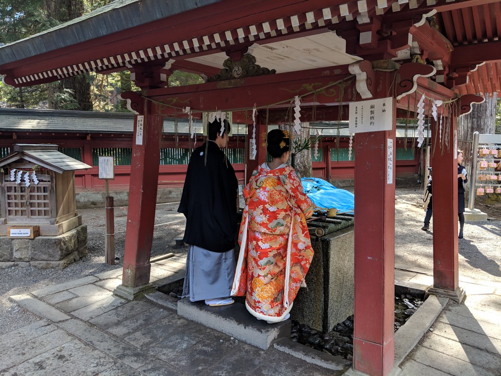 Couple de Japonais en tenue traditionnelle se lave les mains dans la petite fontaine de la zone de prière au sanctuaire Futurasan