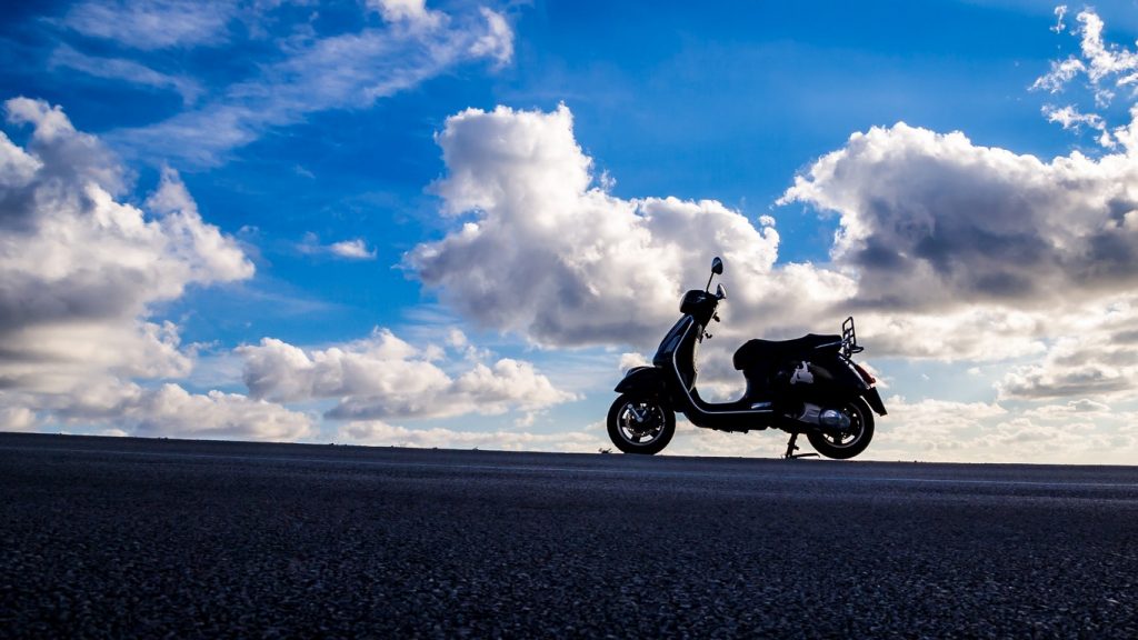Un scooter à contre jour avec des nuages et un ciel bleu dans le fond