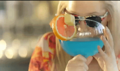 Une femme avec des lunettes de soleil boit discrètement un énorme cocktail bleu