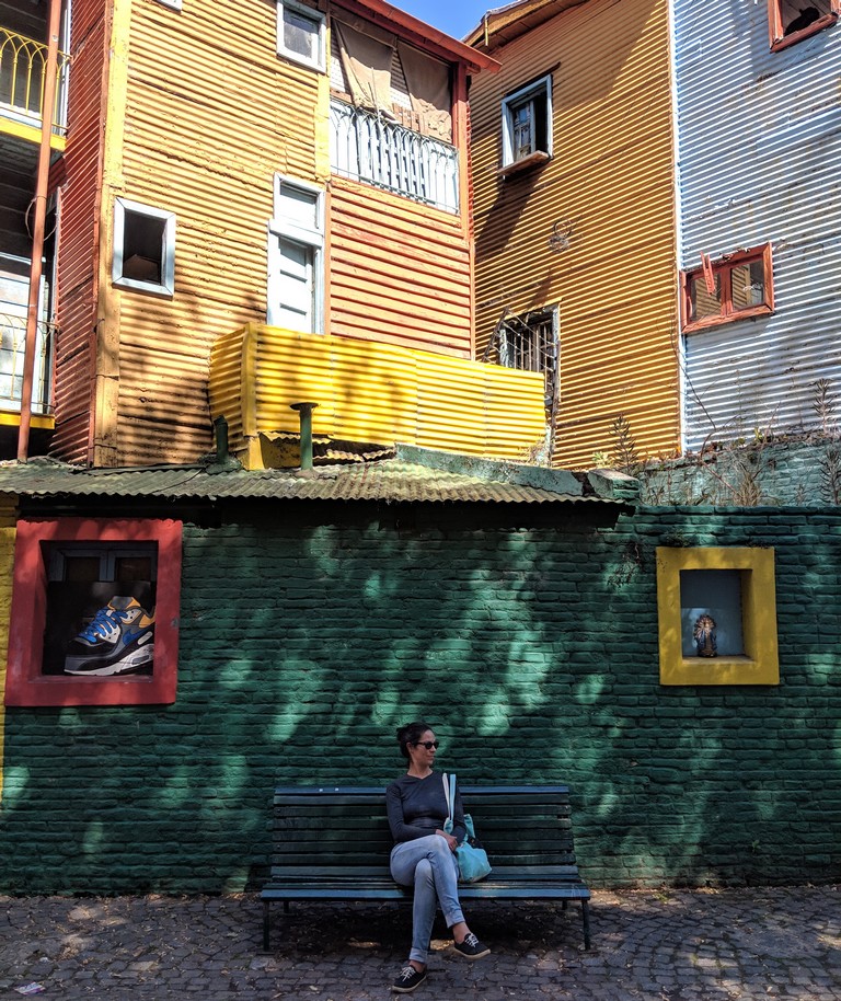 Salomé assise sur un banc devant des façades colorées de la Boca à Buenos Aires