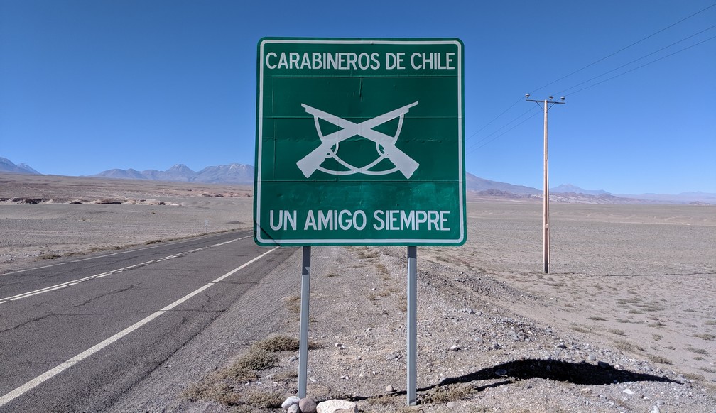 Un panneau sur le bord de la route au milieu du désert, afficant 'Carabineros de Chile, Un Amigo Siempre'