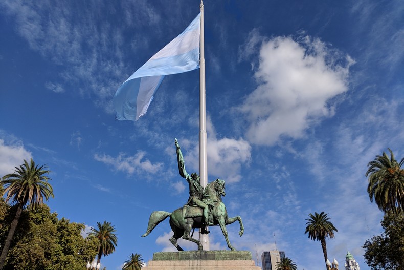 Une statue d'un cavalier devant le drapeau argentin flottant
